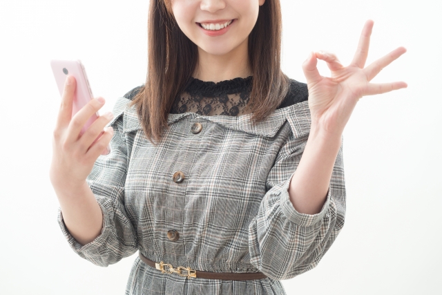 スマホを片手に丸サインをしている女性