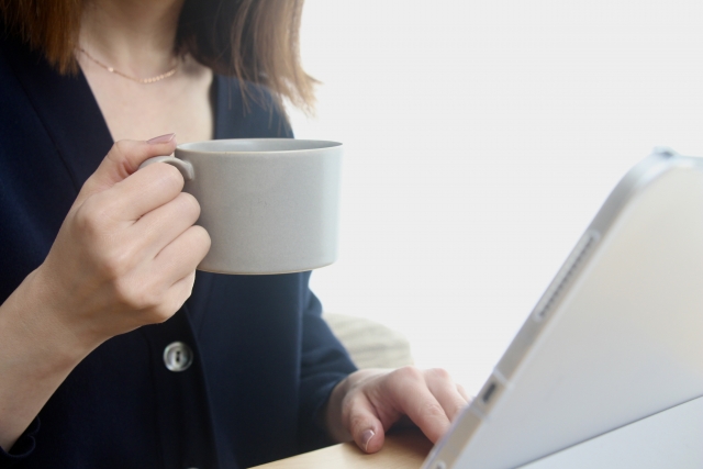 パソコンの前でコーヒーカップを持つ女性