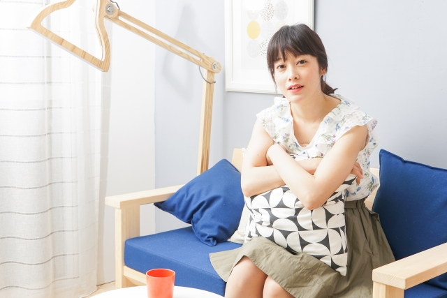 1人、ソファーに乗りクッションを抱いている女性。